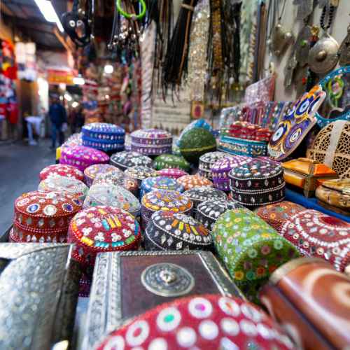 A colorful display of ornately designed boxes and containers at a Marrakech market stall, with a lively background of various wares and shoppers.